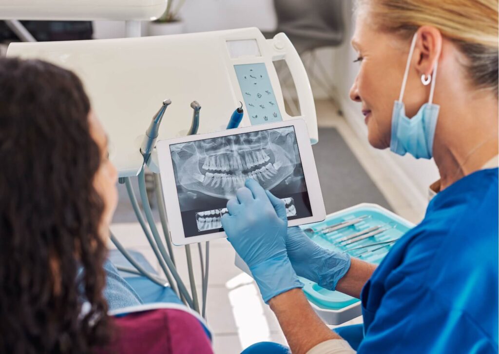 Dentist reviewing dental X-rays with a patient to help decide between a single tooth implant and a dental bridge.